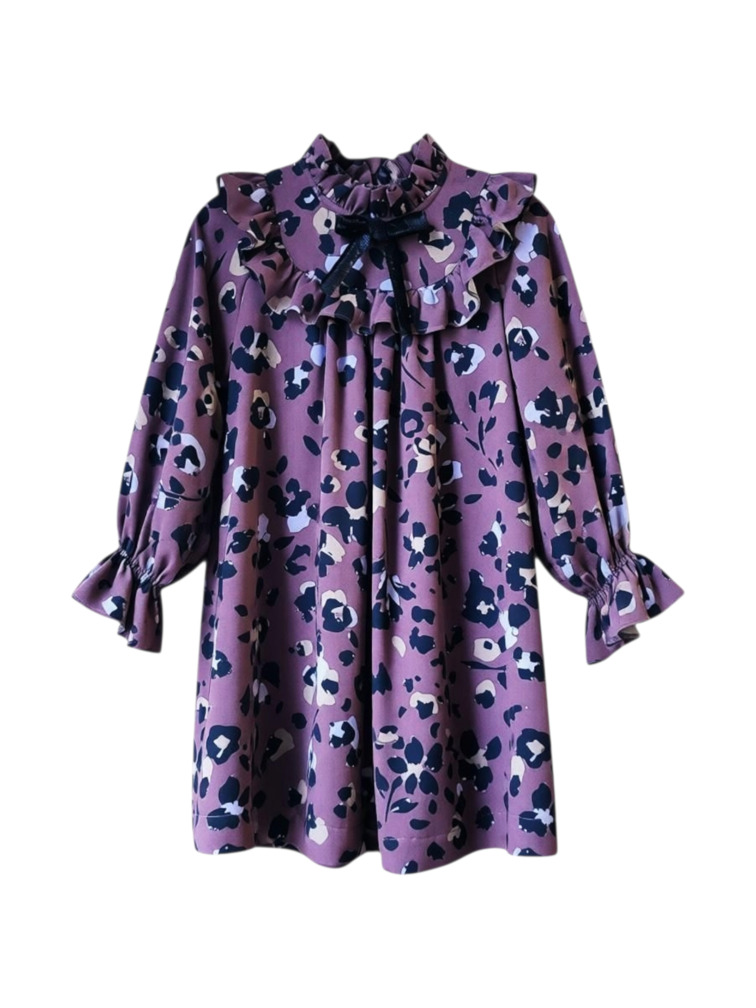 Meiteņu kleita ar raibu apdruku uz violetsārta fona. Kleitai ir volāns ap kaklu un ap pleciem, melna samta bante vidū.